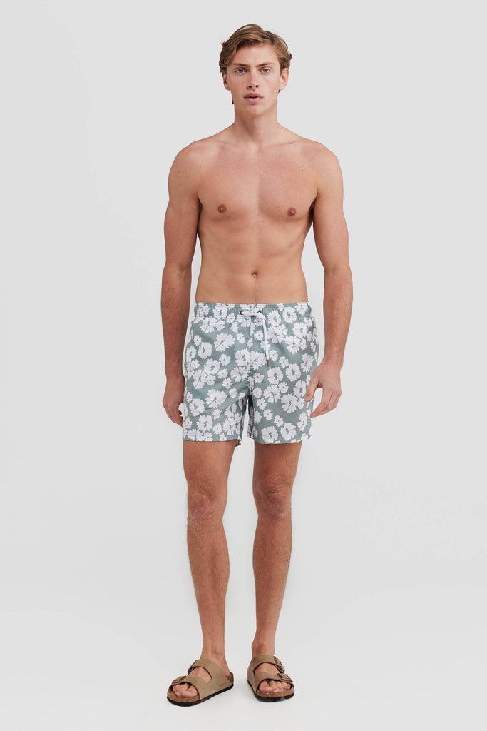 Model wearing sage board shorts with white flowers on them.